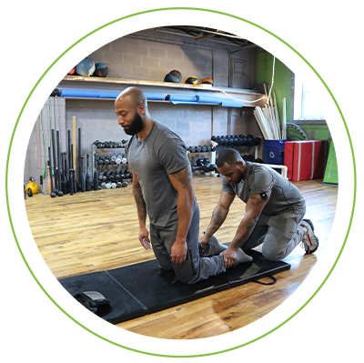 Man helping a teammate do exercises on a mat